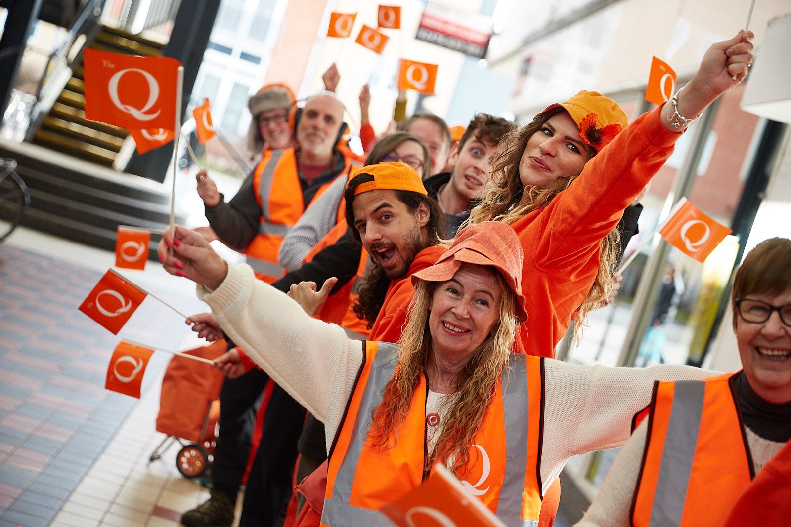 Ornage clad queuers wave flags in shopping arcade